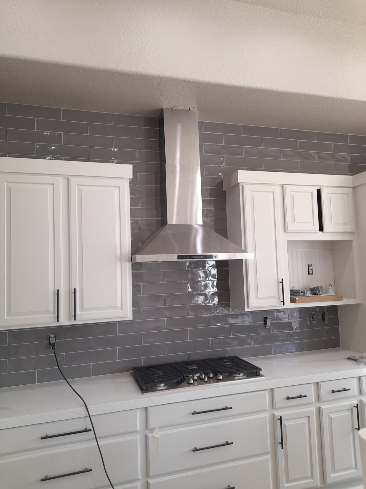 Gray gloss subway tile kitchen backsplash running full height behind a stainless range hood