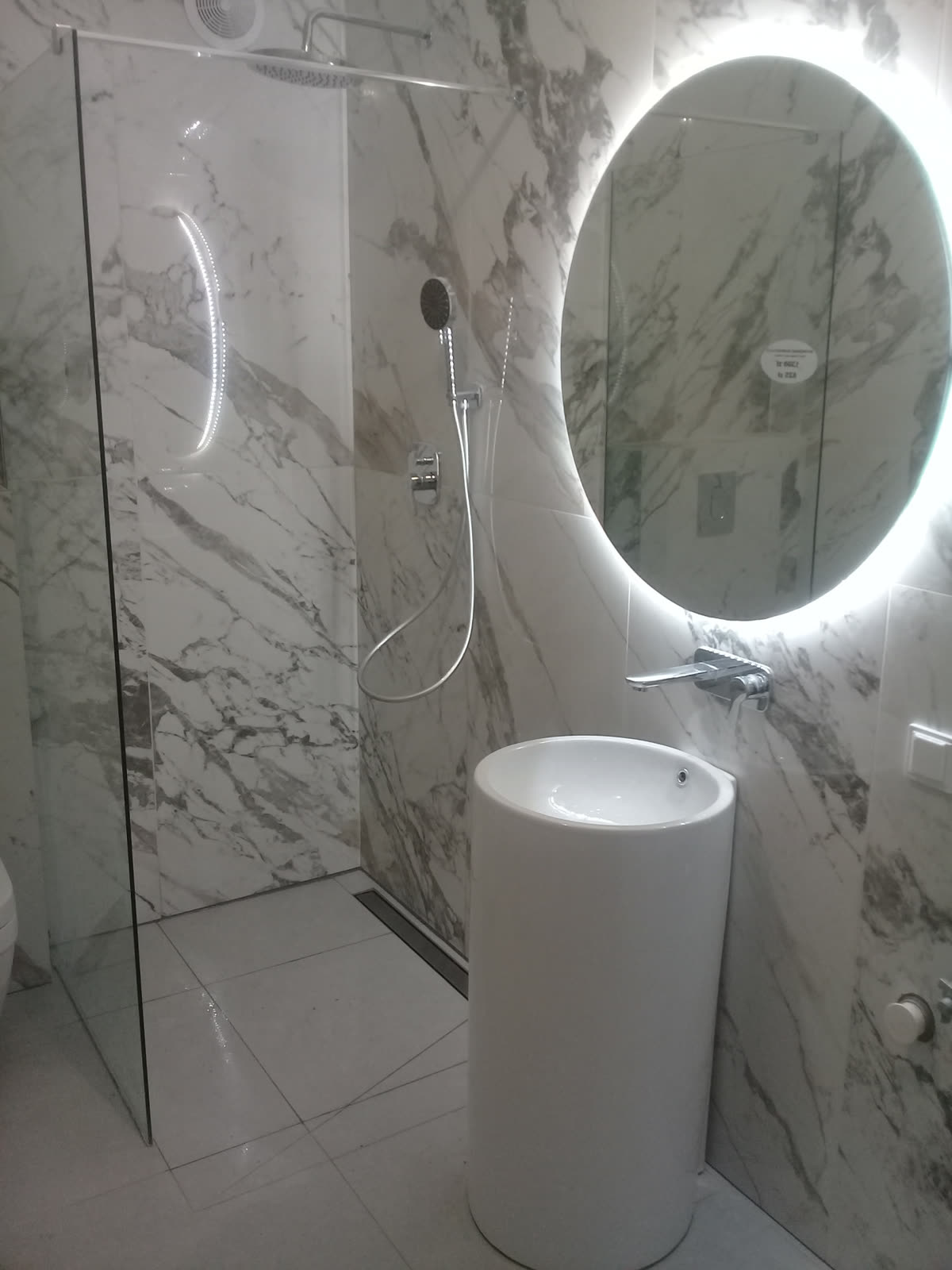 Bathroom with marble-look tiled walls, glass walk-in shower, linear drain and pedestal sink