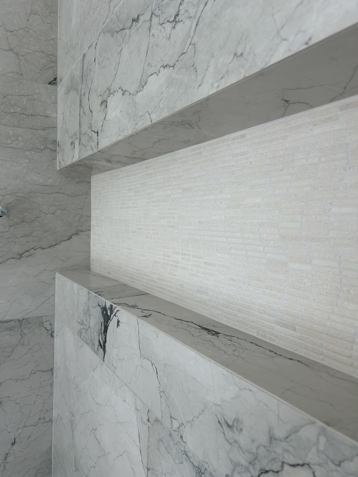 Tiled shower niche with mosaic back and stone shelf in a marble-look porcelain wall